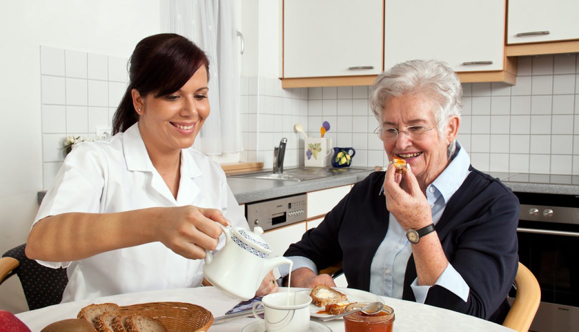 nurse helps elderly woman at breakfast